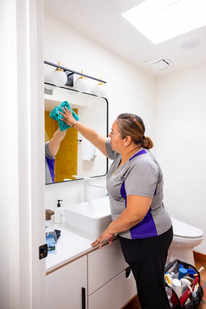 Staff ,member cleaning a mirror at comfort room